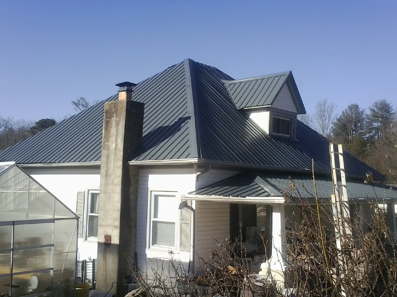 Dark blue standing seam metal roof on a white farmhouse with dormer — Slate & Tile Roof Repair by Roofing Brothers in Corsicana