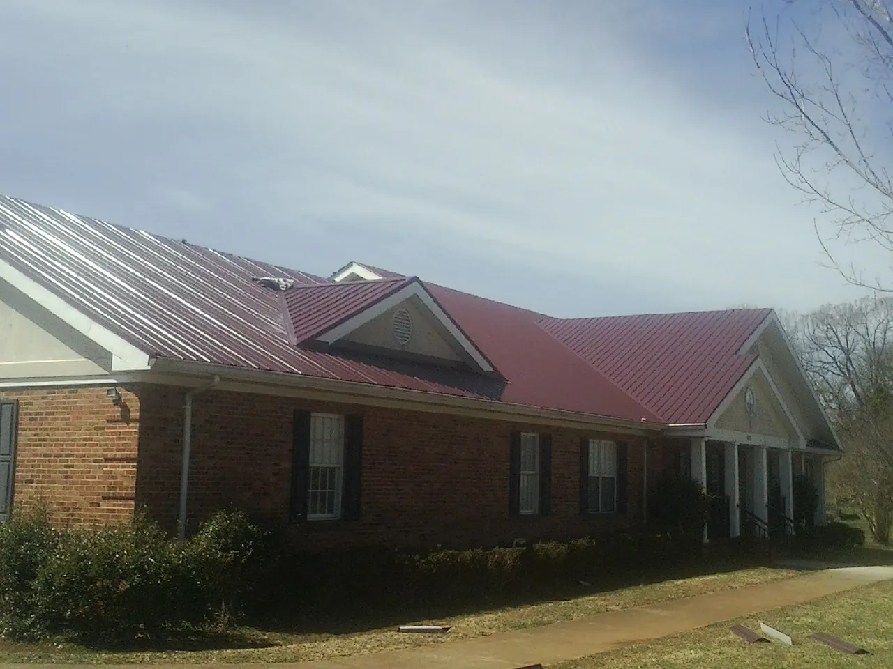 Red metal roof with gabled entries on a long brick building, from a Hail Damage Roof Repair job in Corsicana