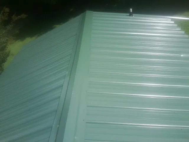 New green metal panels meeting at the ridge of a roof — Flat Roof Repair work by our crew in Corsicana
