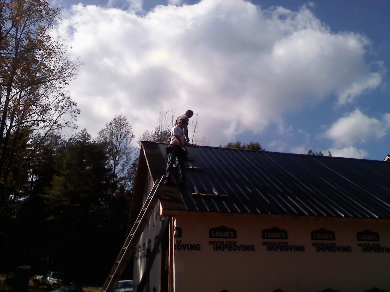 Roofer fastening dark metal panels high against a cloudy sky, from a Roof Inspection job in Corsicana