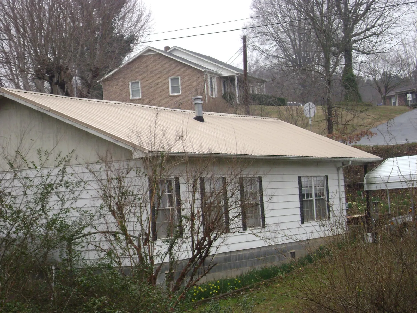 Tan metal roof on a white sided house set into a hillside — Commercial Roofing by Roofing Brothers in Corsicana