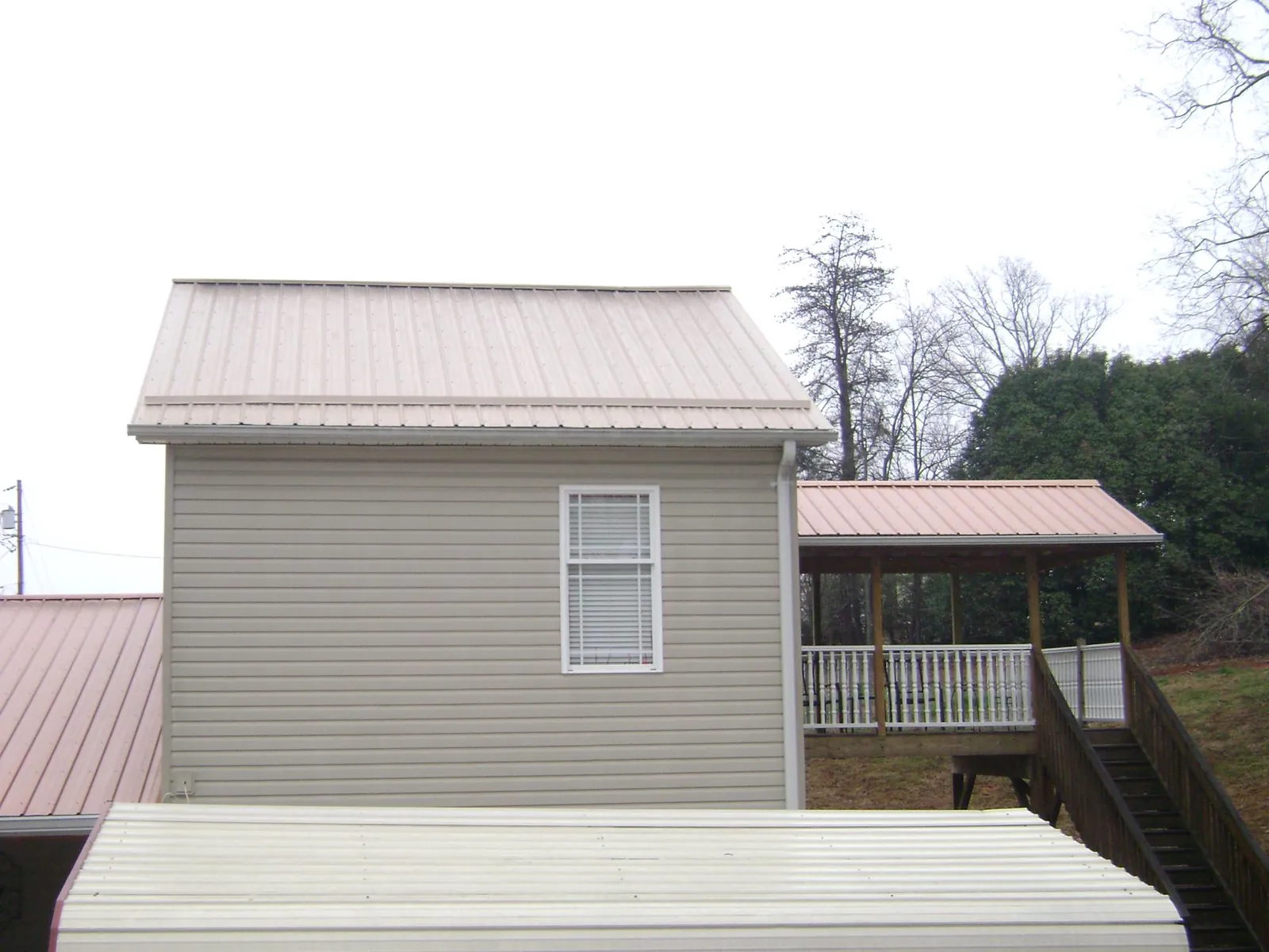 Tan metal roofs on a two story addition and attached porch, from a Roof Replacement job in Corsicana